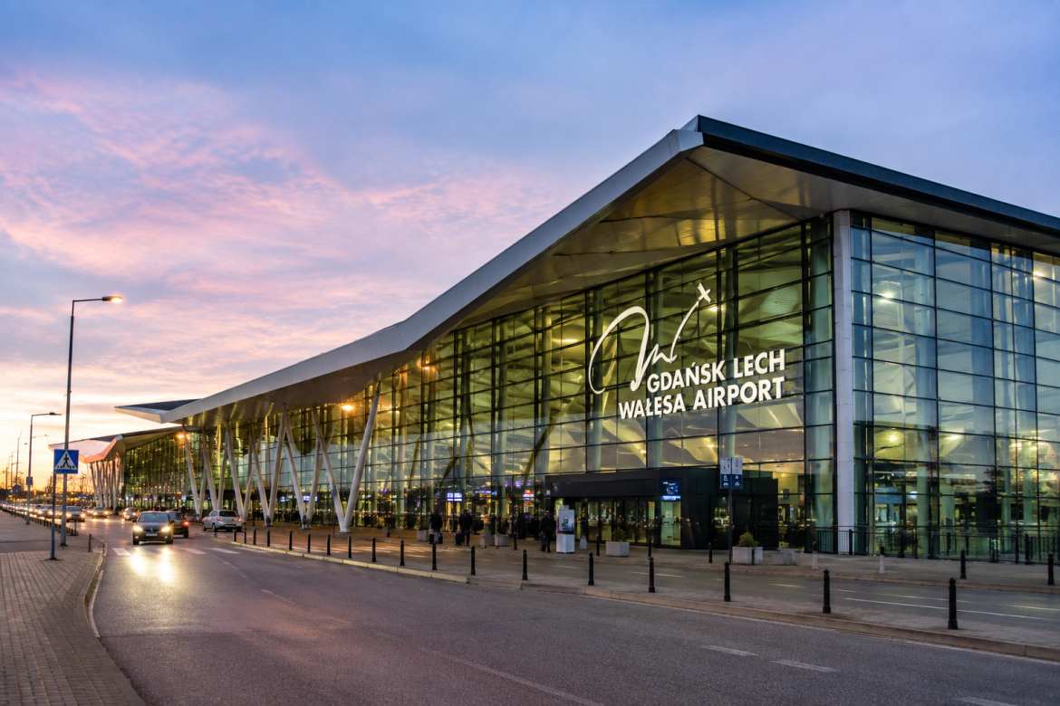 Будівля терміналу міжнародного аеропорту Gdańsk Lech Wałęsa Airport увечері зі скляним фасадом та підсвіткою на тлі рожево-синього неба